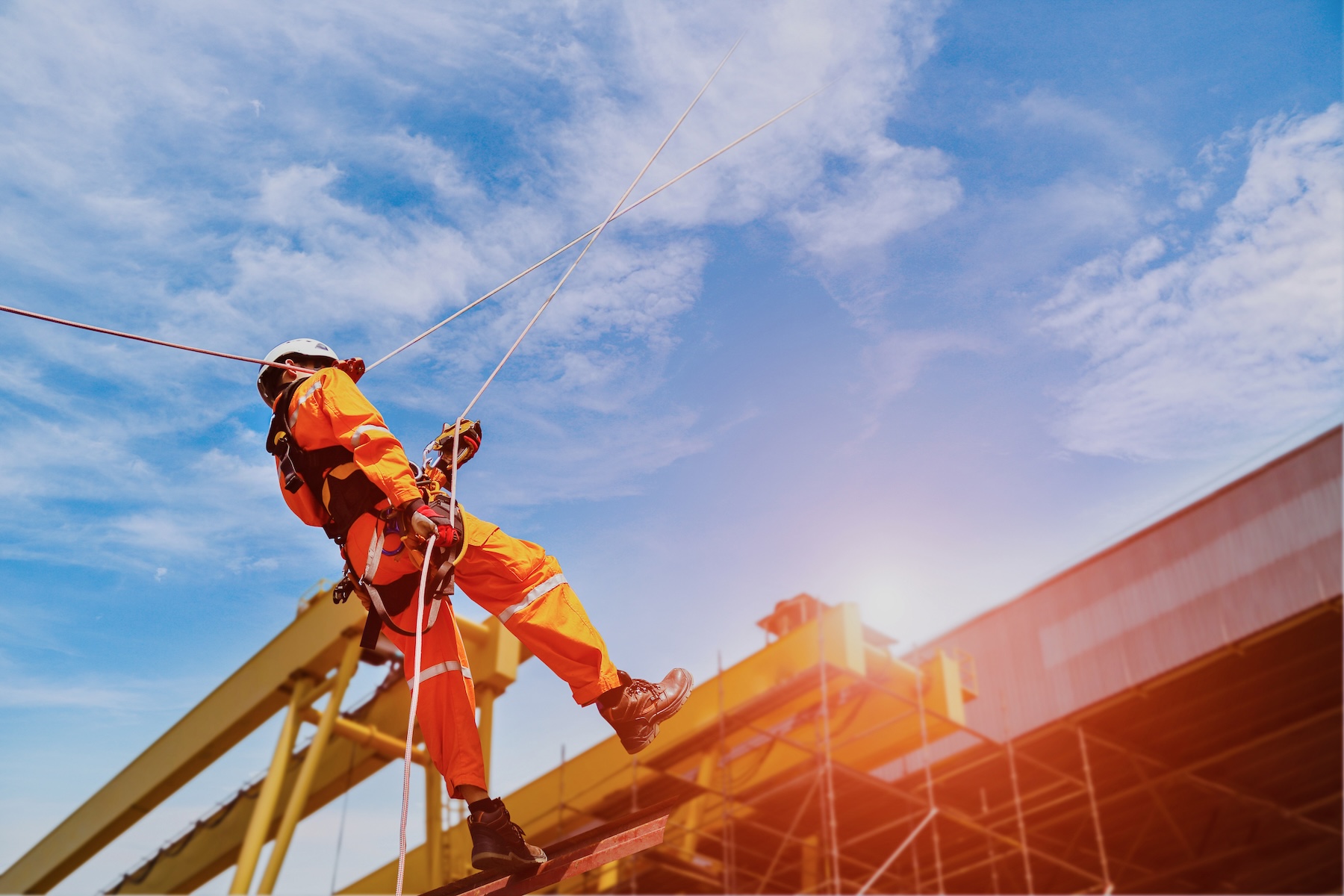 Rope access construction worker wearing full safety body harness with helmet protection hanging off a factory roof